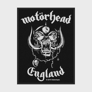 Può includere: Una toppa rettangolare in tessuto bianco e nero con la scritta motorhead in alto e England in basso. Il centro mostra un'illustrazione dettagliata di una creatura con teschio cornuto, una catena e un piccolo ciondolo a croce di ferro.