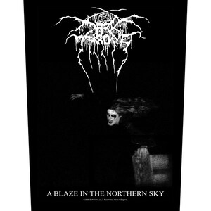 May include: A black and white rectangular fabric patch featuring the Darkthrone logo in a stylized, jagged font at the top. Below, a figure with long hair and face paint is depicted. The text A BLAZE IN THE NORTHERN SKY is printed at the bottom.