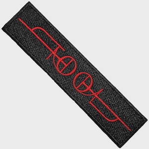 May include: A rectangular black embroidered patch featuring the word TOOL stitched in bright red thread. The lettering is stylised with a horizontal line running through the centre of the characters, creating a bold and distinct graphic design.