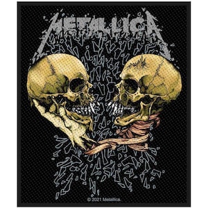 May include: Black patch with the band name "Metallica" in silver, above two yellow skulls facing each other. The skulls have visible teeth and are surrounded by a shattered glass effect. The patch is bordered in black.