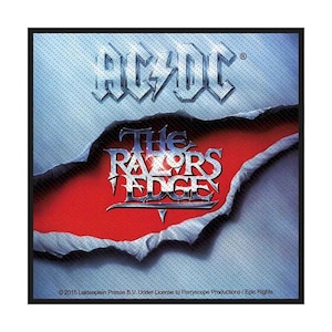 Puede incluir: Un parche de tela cuadrado con el logotipo de AC/DC en plata metálica sobre el texto THE RAZORS EDGE en letras plateadas. El diseño muestra un fondo azul texturizado rasgado que revela un centro rojo sólido. El copyright está abajo.