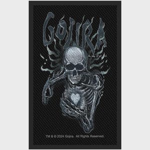 Könnte beinhalten: Ein rechteckiger schwarzer Stoffaufnäher mit einer weißen Grafik eines Skeletts, das ein leuchtendes Herz hält. Der Text GOJIRA erscheint in einer stilisierten Schrift über dem Skelett, zusammen mit den Worten the way of all flesh und TM 2024.
