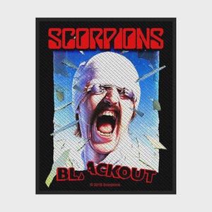 May include: A rectangular patch featuring the Scorpions Blackout album art. It shows a person with a white bandage wrapped around their head, wearing glasses, with their mouth wide open. The background is blue with shattered glass shards.