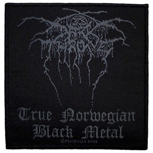 May include: Black square patch with gray text and design. The text reads "True Norwegian Black Metal" in a gothic font. The design is a stylized, intricate emblem. The patch is from Peaceville 2003.
