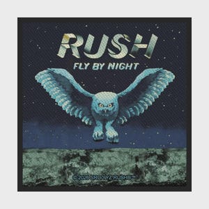 Op de afbeelding: Een vierkante patch met een blauwe uil met gespreide vleugels die vliegt tegen een donkere sterrenhemel. De tekst RUSH en FLY BY NIGHT staat in het wit boven de uil. De onderkant toont een getextureerd landschap met de tekst 2026 SRO/YYZ RUSH.
