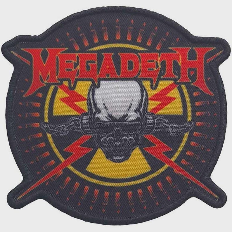 May include: A circular embroidered patch featuring the red text MEGADETH across the top. The centre displays a white skull with black shading, wearing dark sunglasses, set against a yellow radiation symbol and red lightning bolts on black.