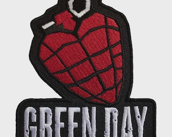 Peut inclure: Un écusson brodé représentant une grenade à main en forme de cœur rouge avec des lignes de grille noires et une goupille blanche. Sous la grenade, une base rectangulaire noire affiche le texte blanc GREEN DAY dans une police sans empattement.