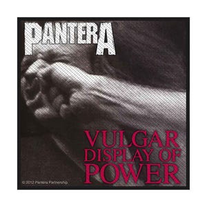 May include: Black square patch featuring the band name "PANTERA" in white, above the text "VULGAR DISPLAY OF POWER" in red. The image includes a grayscale photo of a person's face and hands.
