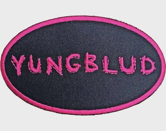 May include: An oval-shaped embroidered patch featuring a black fabric background with a bright pink stitched border. The text YUNGBLUD is embroidered in the centre in a matching bright pink thread with a stylised, slightly distressed font style.