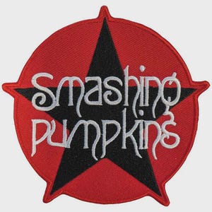 May include: A circular embroidered patch featuring a black five-pointed star on a red background. The text "Smashing Pumpkins" is stitched in white across the center of the star in a stylized, flowing font with a distinct, decorative appearance.