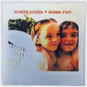 May include: A square fabric patch featuring the Smashing Pumpkins Siamese Dream album cover art. The image displays two young children smiling, with the text Smashing Pumpkins and Siamese Dream printed in a reddish-brown font at the top.