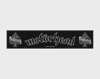 Peut inclure: Un tapis de bar rectangulaire noir avec le texte blanc "motörhead" au centre. Sur les côtés gauche et droit, un graphique de pique blanc contient le texte "ACE OF SPADES". Le texte "© 2010 Motorhead" est imprimé en petites lettres blanches sous le logo.
