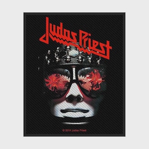 Può includere: Una toppa rettangolare in tessuto con una grafica in bianco e nero di un volto che indossa un copricapo borchiato e occhiali da sole scuri con riflessi rossi. Il testo Judas Priest appare in lettere rosse sopra, con 2014 Judas Priest in basso.