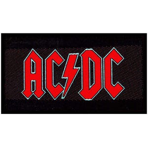 May include: A rectangular black fabric patch featuring the red AC/DC logo with a central lightning bolt. The letters and bolt are outlined in a light blue border, set against a dark, textured background that fills the rectangular shape.