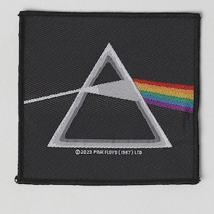 Könnte beinhalten: Ein quadratischer, schwarzer Aufnäher mit einem weißen dreieckigen Prisma, in das links ein weißer Lichtstrahl eintritt und rechts ein Regenbogenspektrum austritt. Der Text lautet ©2023 PINK FLOYD (1987) LTD.
