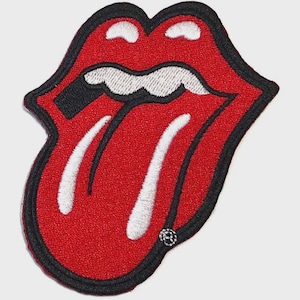 Puede incluir: Un parche bordado que presenta una boca roja estilizada con dientes y lengua blancos, delineado con hilo negro grueso. El diseño muestra un par de labios con la boca abierta, exhibiendo una lengua y dientes prominentes en un estilo gráfico.