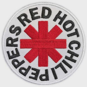 May include: A circular embroidered patch featuring a white background with a central red asterisk-like symbol. The black text "RED HOT CHILI PEPPERS" is stitched in a circular pattern around the red symbol, with a white stitched border edge.