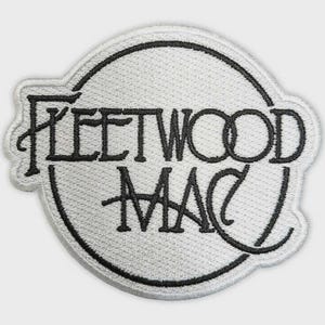 May include: A circular embroidered patch featuring a white background with black stitching. The text Fleetwood Mac is embroidered in a stylized black font across the center, enclosed within a thin black circular border on a textured fabric surface.