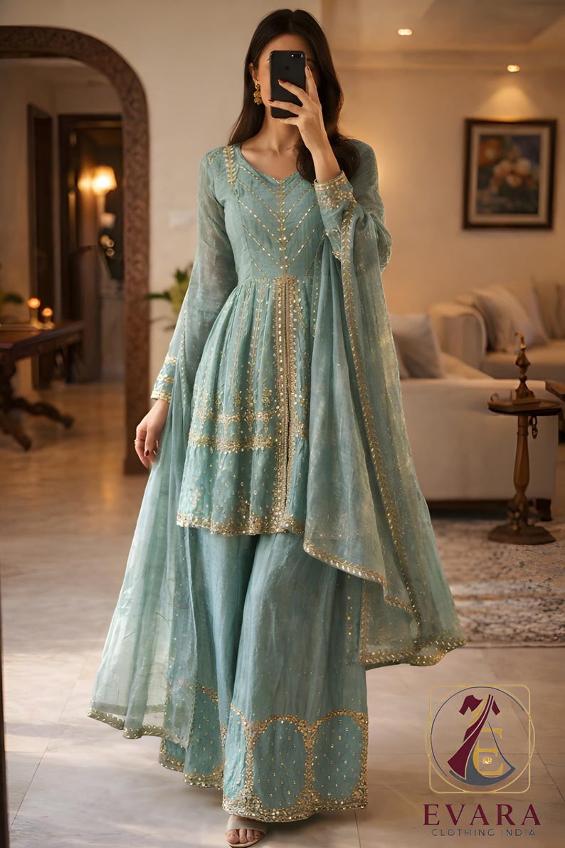 May include: A light blue ensemble featuring a tunic top and wide-leg pants, embellished with gold accents. The outfit includes a matching sheer scarf. The clothing is from Evara Clothing.
