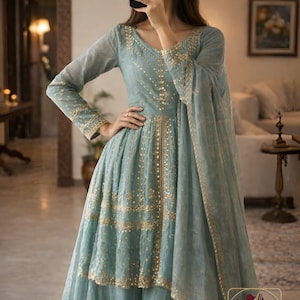May include: A light blue formal dress with gold embroidery. The dress features a V-neck, long sleeves, and a flowing skirt. The dress is part of a two-piece set and includes a matching scarf. The dress has the text "EVARA CLOTHING NO 4".