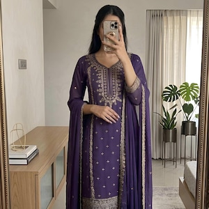 May include: A purple salwar kameez set with gold embroidery. The long-sleeved tunic and matching pants are adorned with intricate gold patterns. The set includes a matching dupatta. The image also shows the "EVARA CLOTHING INDIA" logo.