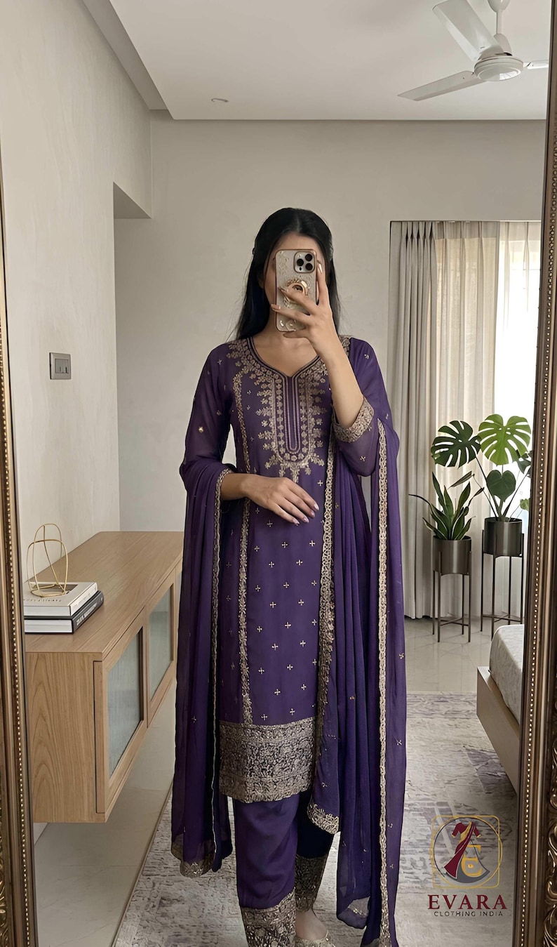 May include: A purple salwar kameez set with gold embroidery. The long-sleeved tunic and matching pants are adorned with intricate gold patterns. The set includes a matching dupatta. The image also shows the "EVARA CLOTHING INDIA" logo.