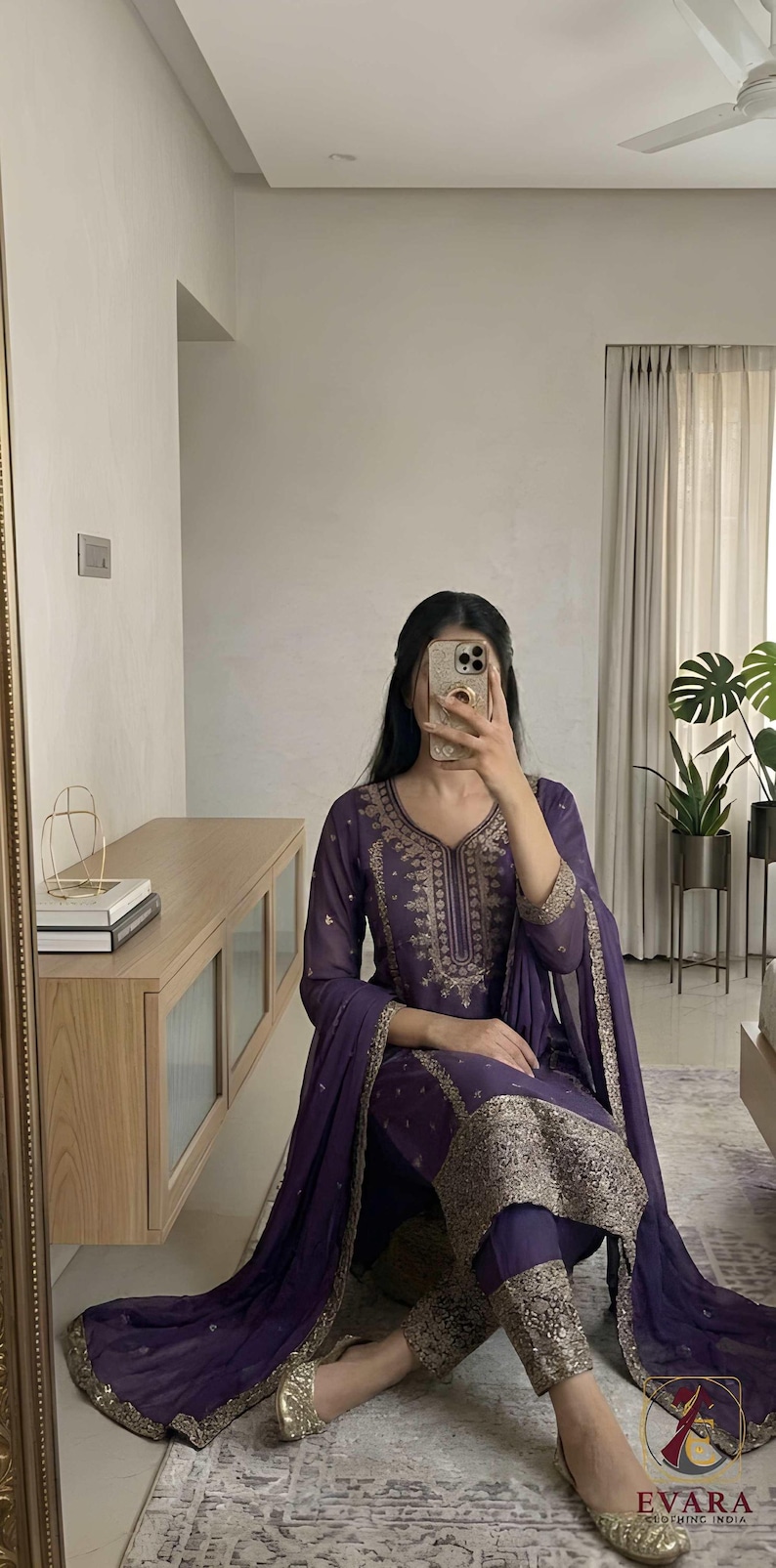 May include: A purple embroidered salwar kameez set. The ensemble features intricate gold embroidery on the neckline, sleeves, and pant hems. The outfit includes a matching dupatta and pants. The clothing is made of a flowing fabric.