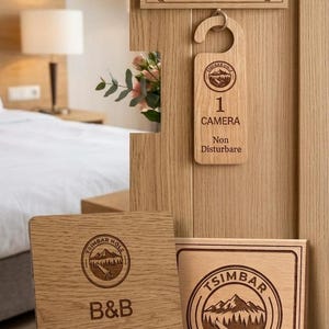 Può includere: Un set di insegne per hotel in legno chiaro che include una targa rettangolare con il numero 10, un cartello da porta con il testo 1 CAMERA Non Disturbare, un cartello quadrato B&B con dettagli WiFi e un portachiavi circolare con chiave.
