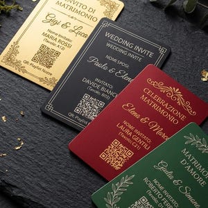 Può includere: Quattro cartoncini rettangolari di invito a nozze in oro, nero, rosso e verde, con bordi floreali, nomi degli sposi, nome dell'invitato, numero del tavolo e un codice QR per una playlist. Una penna dorata poggia su un supporto in legno.