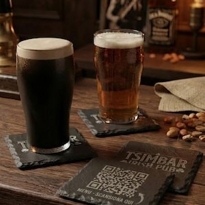 May include: Two square slate coasters with rough edges, each featuring a white engraved QR code and the text TSIMBAR IRISH PUB MENU - SCANSIONA QUI. One coaster sits under a dark stout with foam, the other under a glass of golden amber beer.