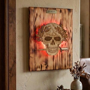 Può includere: Opera d'arte da parete in legno raffigurante un teschio scolpito con una corona d'alloro e un pugnale. L'opera è montata su un pannello di legno tinto con il numero romano MCMXV. Il teschio è illuminato da una luce rossa.