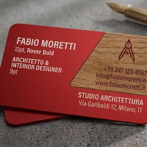 Op de afbeelding: Een rechthoekig visitekaartje met een rode matte afwerking aan de linkerkant en een houtnerftextuur aan de rechterkant. De tekst luidt FABIO MORETTI, ARCHITETTO & INTERIOR DESIGNER, STUDIO ARCHITETTURA, Via Garibaldi 12, Milano, IT, en contactgegevens.