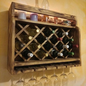 Peut inclure: Un casier à vin en bois rustique avec un porte-bouteilles en losange et une rangée de porte-verres. Le casier est rempli de bouteilles de vin et possède une étagère avec des bougies et une bouteille. Le casier est fixé au mur.