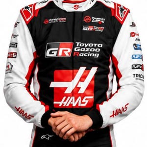 Puede incluir: Una persona con un traje de carreras negro, blanco y rojo con los logotipos de Toyota Gazoo Racing y Haas. El traje tiene el n&uacute;mero 87 en los pantalones. La persona sonr&iacute;e.
