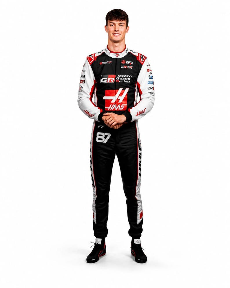 Puede incluir: Retrato de cuerpo entero de una persona con un mono de carreras negro, con detalles en blanco y rojo, y logotipos de Toyota Gazoo Racing y Haas. El n&uacute;mero 87 es visible en el mono. La persona est&aacute; de pie, con las manos juntas.