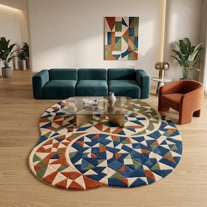 May include: A large, irregularly shaped area rug featuring a geometric pattern of triangles in shades of deep blue, burnt orange, sage green, and cream. The rug has a textured, tufted surface and is positioned on a light-colored wooden floor.