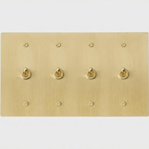 Può includere: Una placca interruttore rettangolare in ottone con quattro interruttori a levetta e otto teste di vite. La placca ha una finitura spazzolata ed è montata su uno sfondo bianco. Gli interruttori a levetta sono color oro.