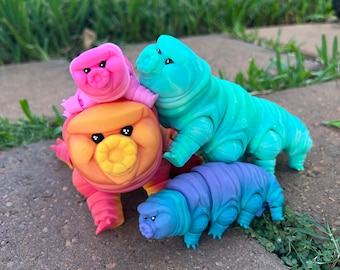 May include: Four colorful, segmented, plush toys resembling worms. The toys are arranged in a playful pose, with one standing on its hind legs and the others leaning on it. The toys are made of soft, textured fabric and have a whimsical, cartoonish appearance.