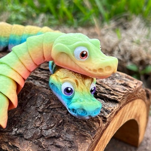 May include: Two colorful, segmented, toy crocodiles with rainbow-colored scales. The top crocodile is green and yellow, and the bottom crocodile is blue and green. The crocodiles are on a brown, wooden log.