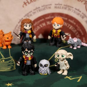 May include: A collection of Harry Potter character figurines, including Harry, Hermione, Ron, Dobby, and Hedwig. The figures are in their Hogwarts uniforms, with wands and other accessories. An orange cat and a gray rat are also present.