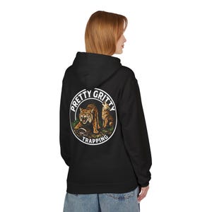 May include: Black hooded sweatshirt with a circular graphic on the back. The graphic features two wildcats and the words "PRETTY GRITTY TRAPPING" in a white circular border. The sweatshirt is worn by a person.