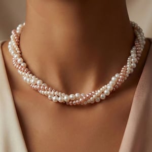 Könnte beinhalten: Mehrsträngige Perlenkette mit weißen und rosafarbenen Perlen. Die Halskette ist um den Hals einer Person drapiert und zeigt das elegante Design und die Farbvariationen. Die Perlen sind in verschiedenen Größen.