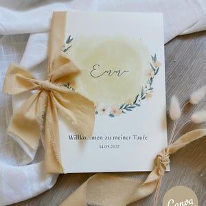 Könnte beinhalten: Eine rechteckige Karte mit einem hellgelben Aquarellkreis und einer Blumenkranz-Illustration. Der Name Emma ist in schwarzer Schreibschrift gedruckt, darunter steht der Text Willkommen zu meiner Taufe und das Datum 14.05.2027. Ein ausgefranstes beiges Band ist an der linken Seite gebunden.