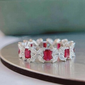May include: A silver-toned eternity band featuring alternating rectangular red gemstones and marquise-cut clear stones. The ring displays a repeating pattern of vibrant red rectangular stones set between pairs of sparkling white marquise-cut stones.