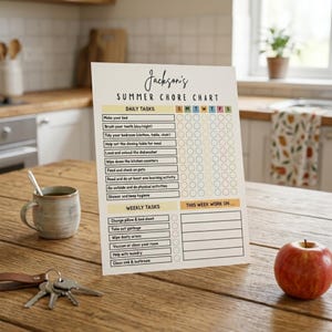 Puede incluir: Un cuadro de tareas titulado "Jackson's SUMMER CHORE CHART" con tareas diarias y semanales. El cuadro est&aacute; sobre una mesa de madera con una taza, llaves y una manzana roja. El cuadro incluye tareas como hacer la cama y sacar la basura.