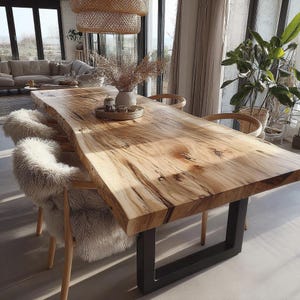 May include: A large, natural wood dining table with a live edge, supported by a black metal base. The table is surrounded by wooden chairs, some with fluffy white seat covers. A vase of dried flowers sits on the table, creating a warm, inviting atmosphere.