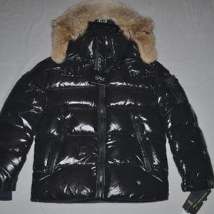 May include: A glossy black puffer jacket with a fur-trimmed hood. The jacket features a full-length zipper, multiple pockets, and a SAM tag. The cuffs are dark blue. This winter coat is designed for warmth and style.