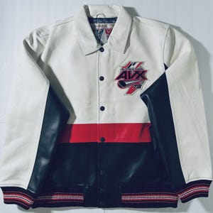 Puede incluir: Chaqueta de cuero blanca, roja y negra con el texto "AVX USA 75" en el pecho. La chaqueta tiene cuello, cierres a presi&oacute;n negros y mangas negras. Los pu&ntilde;os tienen rayas rojas, blancas y negras.