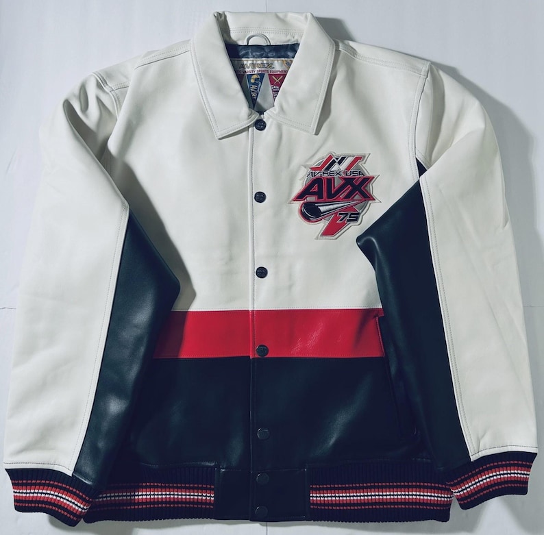 Puede incluir: Chaqueta de cuero blanca, roja y negra con el texto "AVX USA 75" en el pecho. La chaqueta tiene cuello, cierres a presi&oacute;n negros y mangas negras. Los pu&ntilde;os tienen rayas rojas, blancas y negras.