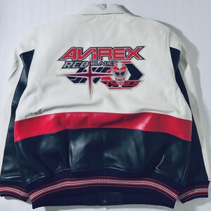 Puede incluir: Chaqueta de cuero blanca, roja y negra con el texto "AVIREX RED BLADES 1923" en la espalda. La chaqueta tiene un dise&ntilde;o tipo bomber con dobladillo y pu&ntilde;os acanalados. El dise&ntilde;o es deportivo y cl&aacute;sico.